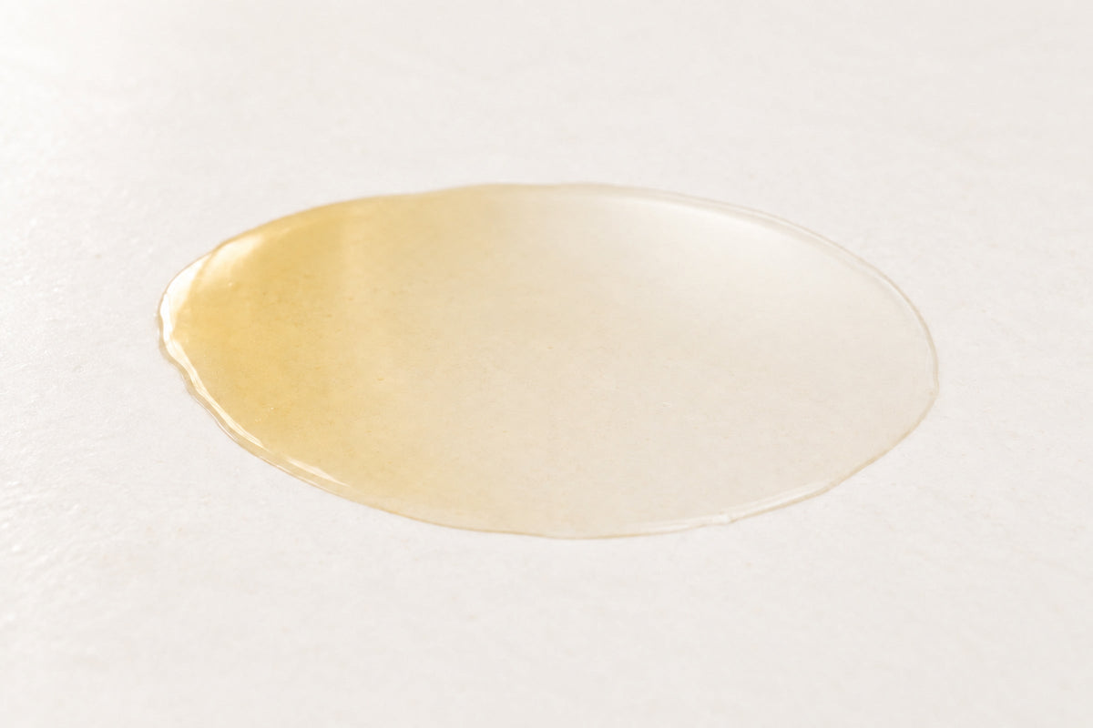 Pale golden oil fading to clear on a warm white surface, representing oil-soluble vitamin C.
